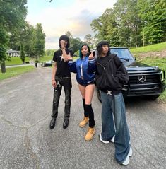 three people standing in front of a black car on the side of the road with one person taking a selfie