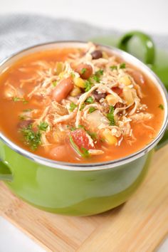 a green bowl filled with soup on top of a wooden cutting board