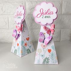 two butterfly shaped boxes with name tags on them, one is pink and the other is white