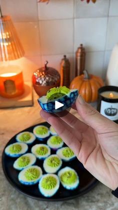 a person holding a small bowl filled with deviled eggs on top of a kitchen counter