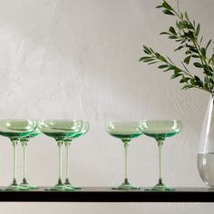 four green wine glasses lined up on a shelf