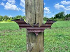 a metal bat hanging on a wooden post in a field with blue sky and clouds