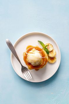 a white plate topped with fruit and ice cream on top of a blue table next to a fork