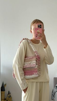 a woman taking a selfie with her cell phone while wearing pajamas and holding a crocheted purse