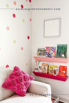 a white couch sitting under a pink and green polka dot wall decal next to a bookshelf