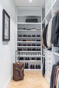 a walk in closet filled with lots of shoes and clothes hanging on the wall next to a suitcase