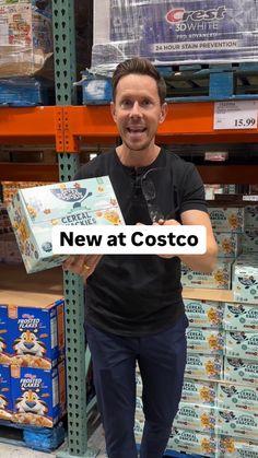 a man standing in front of shelves holding a box with the words new at costo on it