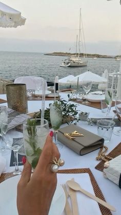 a person is holding up a flower in front of a table set with white linens