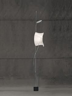 a white sculpture is standing in front of a concrete wall and black potted plant