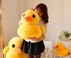 a woman holding two large stuffed ducks in her hands, while standing next to a bed