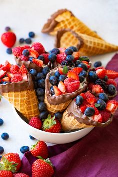 a bowl filled with ice cream and fruit on top of a purple cloth next to two waffle cones