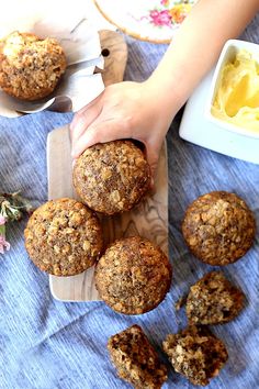 a person reaching for some muffins on top of a wooden cutting board next to other food items