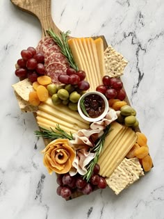 a cheese board with grapes, olives, crackers and other snacks on it