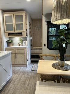 a kitchen and dining area in an rv with wood flooring, white walls and cabinets