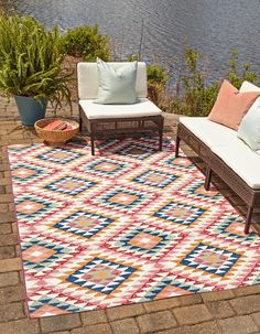 an outdoor area with two chairs and a rug on the ground next to some water