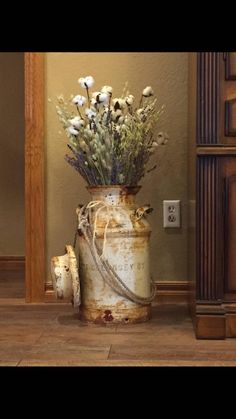 an old rusted can with flowers in it sitting on the floor next to a mirror