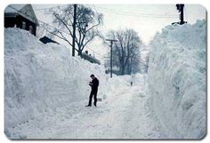 a person standing in the middle of a snow covered street with piles of snow on both sides