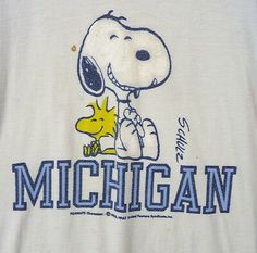 a white shirt with a snoopy dog on it's chest and the word michigan written in blue