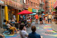 people are sitting and standing on the sidewalk in front of buildings with colorful chalk drawings