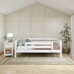 a white day bed sitting on top of a wooden floor next to a potted plant