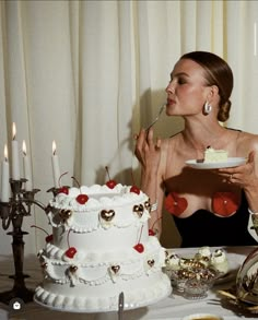 a woman sitting at a table in front of a white cake with cherries on it