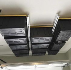 four black bins are hanging from the ceiling in a room with white walls and overhead lighting