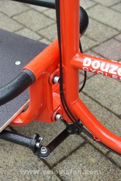 an orange bicycle parked on top of a brick sidewalk next to a skateboard rack