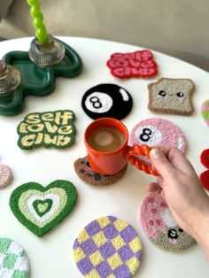 a person holding a coffee cup in front of some crocheted coasters on a table