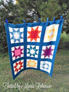 a blue quilt hanging from the side of a tree with stars on it in front of some trees