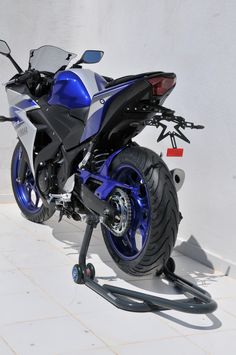 a blue and silver motorcycle parked on the side of a white wall with wheels attached to it