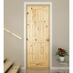 a wooden door sitting in the middle of a room next to some stairs and a vase with flowers