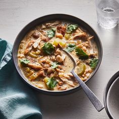 a bowl of soup with meat and vegetables on the table next to a glass of water