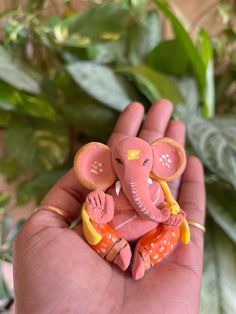 a small pink elephant sitting on top of a person's hand next to a green plant