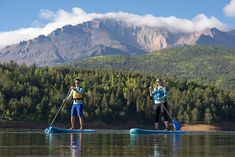 two people on paddle boards paddling in the water with mountains in the back ground