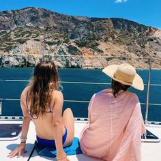 two women in bikinis sitting on the back of a boat looking out to sea