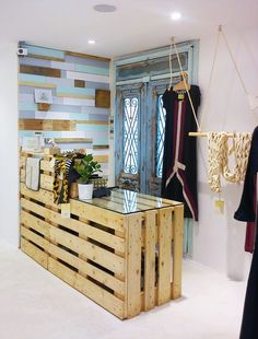 a room with wooden pallets and clothes hanging on the wall, including a glass top counter