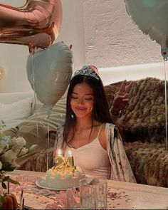 a woman sitting in front of a birthday cake with candles on it and balloons behind her