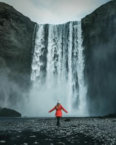 a woman standing in front of a waterfall with her arms spread out to the side