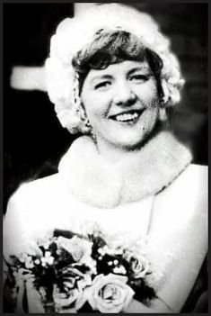 an old black and white photo of a woman in a wedding dress smiling for the camera