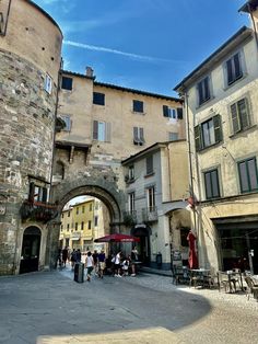 people are walking around in an old european city street with stone buildings and arched archways