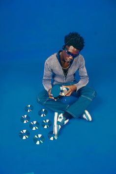 a man sitting on the ground holding a skateboard and several mirrors in front of him