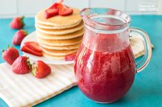 a pitcher filled with red liquid next to stack of pancakes on a blue tablecloth