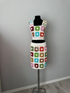 a crocheted dress on a mannequin stand in front of a gray wall