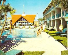 an outdoor swimming pool surrounded by lawn chairs and palm trees with people in the background