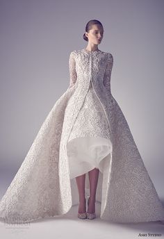 a woman in a white wedding dress with long sleeves and high low skirt, standing against a gray background