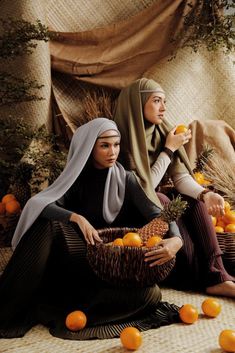 two women sitting on the floor with oranges in their hands and one holding a basket