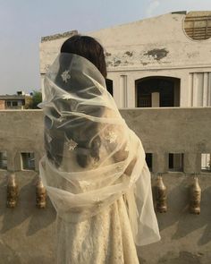 a woman in a white dress and veil standing on a balcony looking out over the city