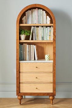 a wooden bookcase with books on top of it and some plants in the corner