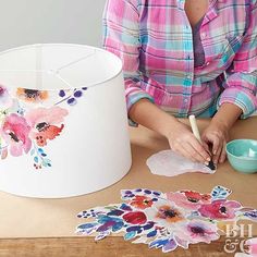 a woman is painting flowers on a white lamp shade with watercolors and paper