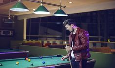 a man standing next to a pool table holding a cue in one hand and looking at his cell phone